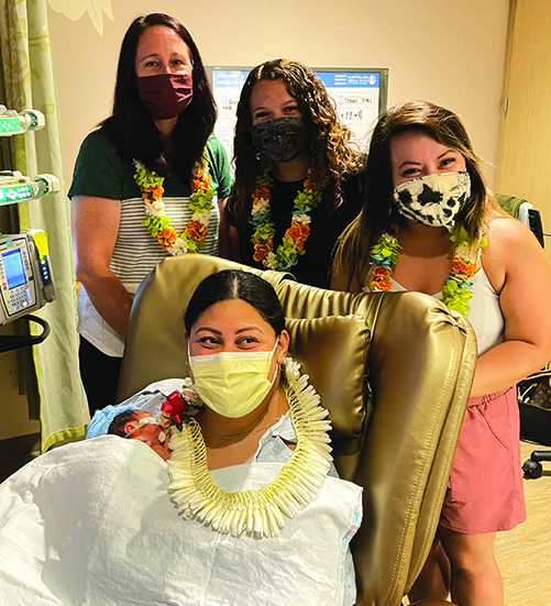 three nurses standing behind hospital chair with new mom and baby