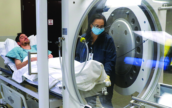 man on hospital bed being rolled into hyperbaric oxygen chamber