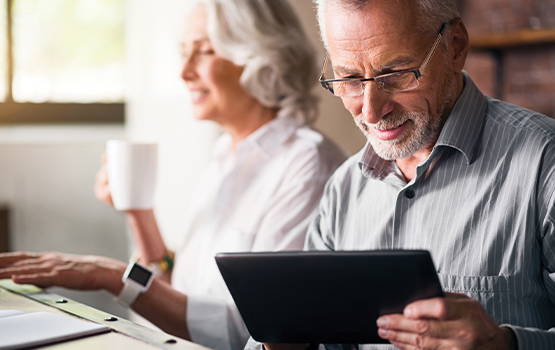 man looking an tablet with woman sitting next to him drinking from a mug