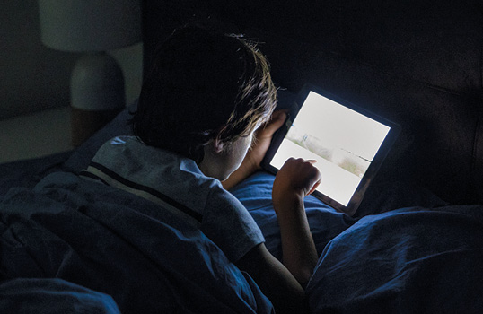 boy sitting in the dark playing on his tablet